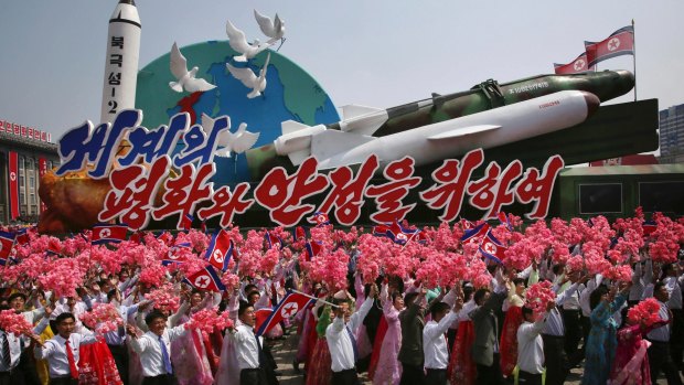 North Koreans wave as they march next to a float display of models of different missiles during a military parade in Pyongyang earlier this month.