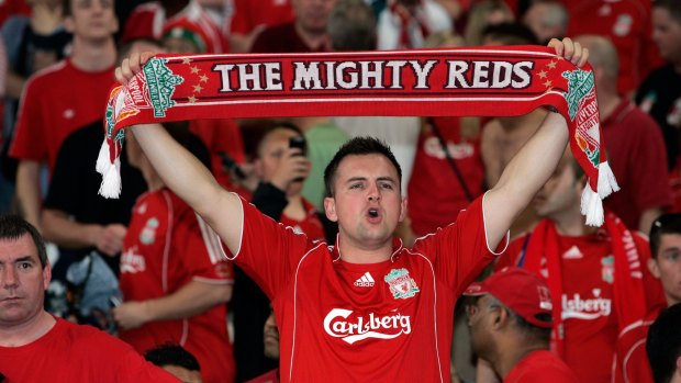 A Liverpool football fan holds up a scarf in the stands during a match.
