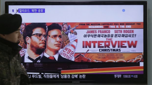 A South Korean soldier walks near a TV screen showing an advertisement for The Interview.