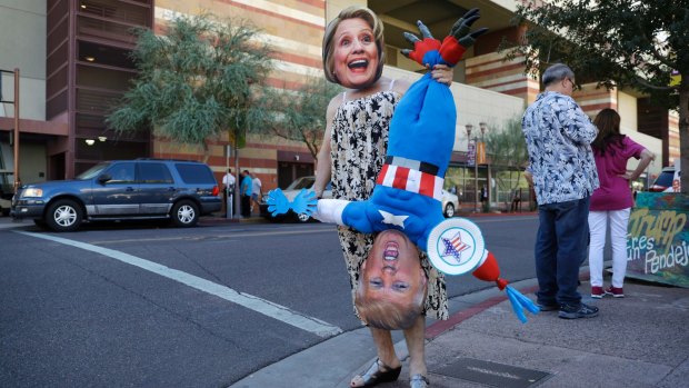 A person wearing a Hillary Clinton mask and holding a Donald Trump effigy stands outside a rally with the Republican presidential candidate.