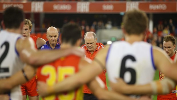 Kangaroos interim coach Darren Crocker and Suns coach Rodney Eade join the players in a huddle on the ground after the game to pay tribute to Phil Walsh.