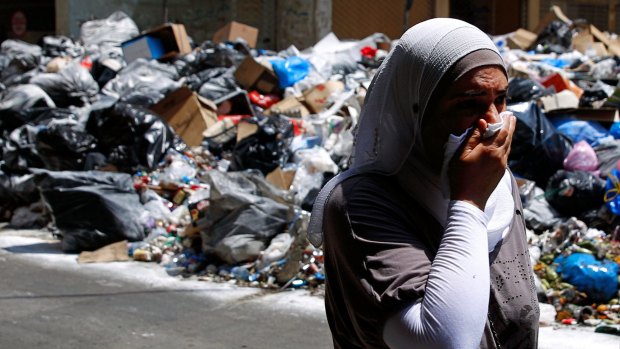 A Lebanese woman covers her nose from the smell as she walks on a street partly blocked by piles of garbage in Beirut on Monday. 