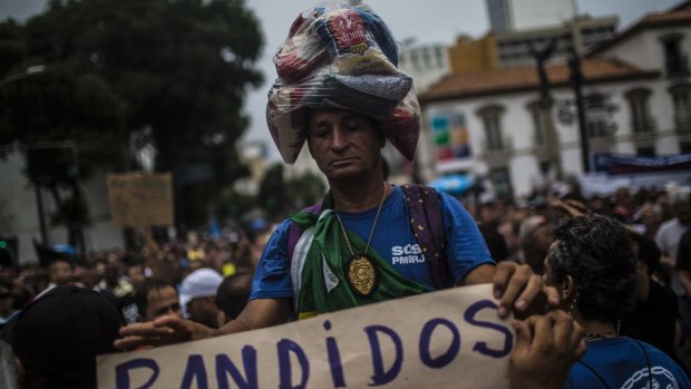 A demonstrator wears packages of rice and beans on his head while holding a sign reading "Thieves" during a protest in Rio de Janeiro.