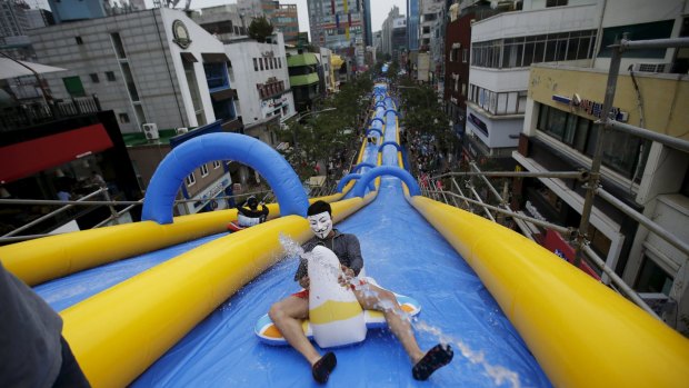 A man wearing a Guy Fawkes mask enjoys a ride on a 350-metre long water slide during 2015 City Silde Festa in central Seoul, South Korea on Saturday.