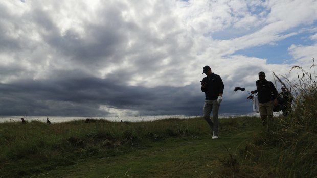 American Jordan Spieth walks between holes during a practice round at Royal Troon, with ominous clouds in the background.