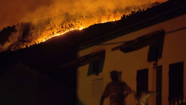 A man on the balcony of a house looks up at a forest fire raging on a hillside above the village of Avelar.