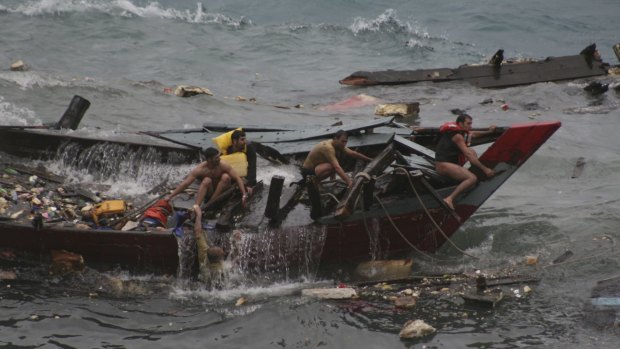 A few stunned men cling to the wreckage of a wooden boat that had been carrying about 90 refugees as it takes on water near Flying Fish Cove on Christmas Island on December 15, 2010. 
