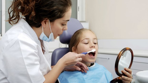 A dentist shows a child how to brush her teeth.