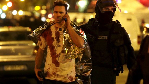 A French policeman assists a blood-covered victim near the La Bataclan concert hall.