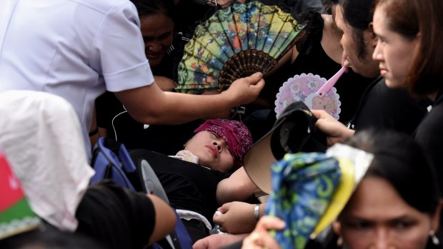 A woman faints outside the Grand Palace in Bangkok waiting for the body of the king.
