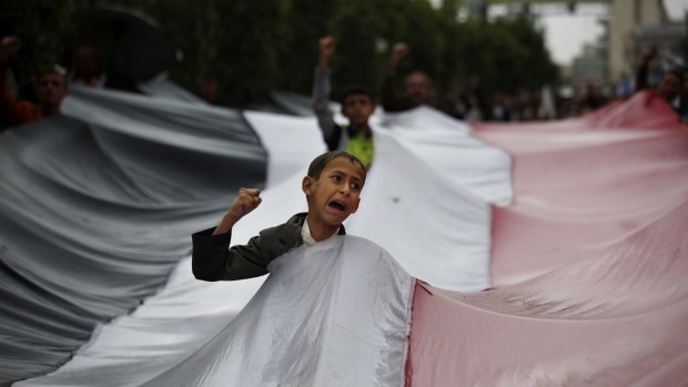 A boy chants slogans through a gap in a national flag raised by Shiite rebels, known as Houthis, during a protest against Saudi-led airstrikes in Sanaa on Friday.