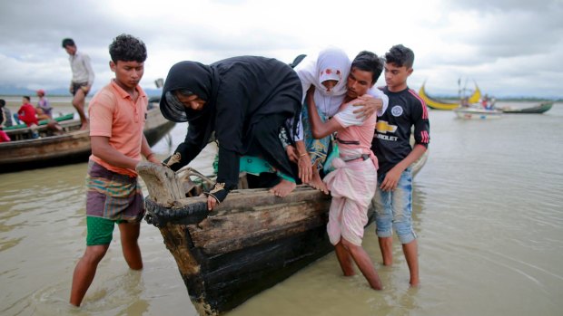 Bangladeshi villagers help two elderly Rohingya women get down from a boat after crossing a canal at Shah Porir Deep, in Teknak, Bangladesh