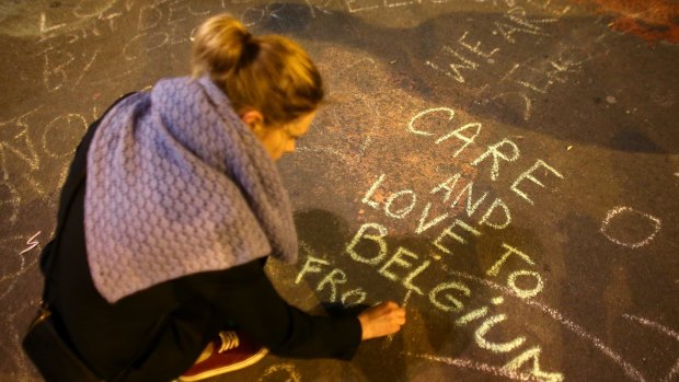 A woman writes a message on the ground as people leave tributes at the Place de la Bourse in Brussels.