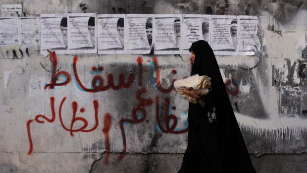 A women carries bread past a wall in the village of Karzakan, Bahrain, with graffiti reading "our demand is the fall of the unjust regime".