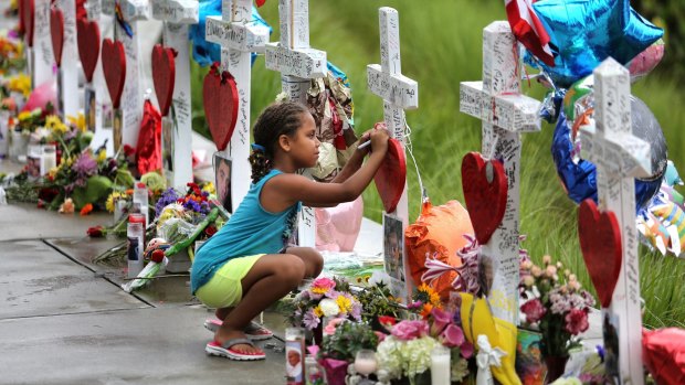 Seven-year-old Mekiha Thomas of Orlando signs one of the 49 crosses at a makeshift memorial outside Orlando Regional Medical Centre.