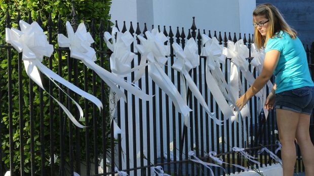 A woman covers the fence of the Emanuel AME Church with nine white ribbons and flowers for the nine victims.