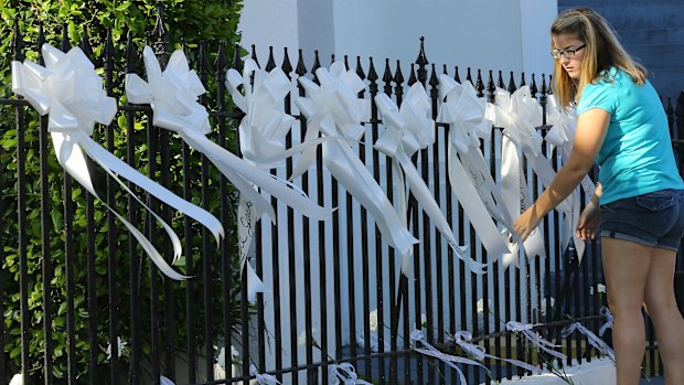 A woman covers the fence of the Emanuel AME Church with nine white ribbons and flowers for the nine victims.