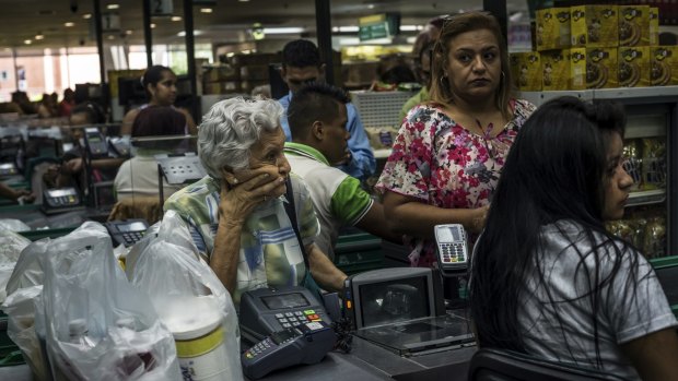 Employees at a private grocery store attend to shoppers who had waited three hours for the store to open so they could buy hard-to-find cooking oil, corn flour, sugar and toilet paper in Caracas, Venezuela, last month. 