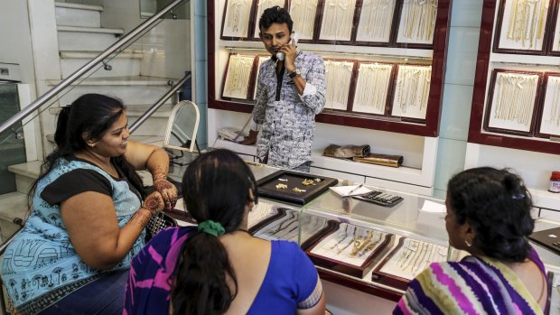 Customers browse gold jewellery as a sales assistant talks on the phone at the store.