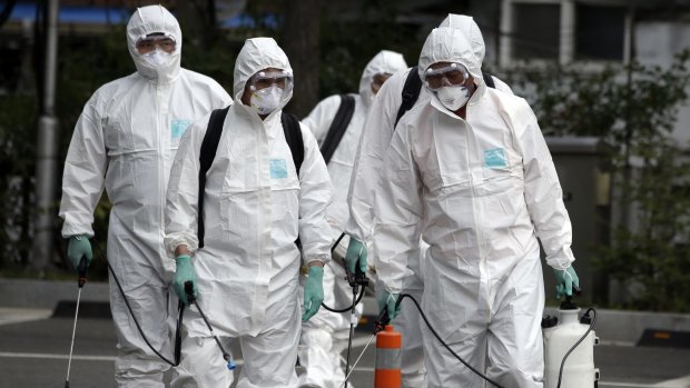 Workers wearing protective gear arrive to spray antiseptic solution as a precaution against the spread of MERS at an art hall in Seoul.