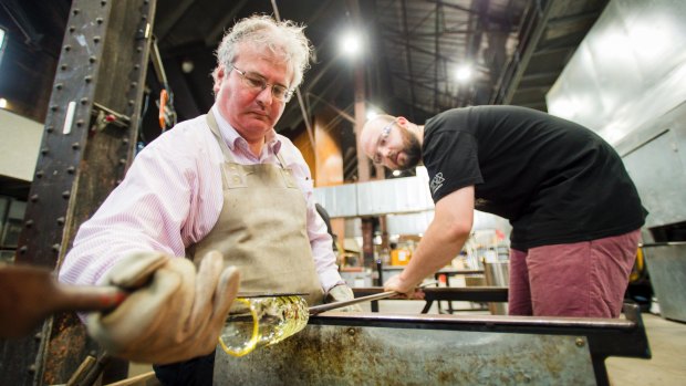 Make Your Own instructor Nick Adams, right, guides <i>Canberra Times</i> reporter Ron Cerabona through the process of making a glass tumbler at Canberra Glassworks.