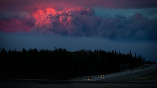 Motorists travel south on Alberta Highway 63 as the setting sun illuminates a huge plume of smoke from wildfires burning in the distance rising over Fort McMurray, Alberta, Canada, on Wednesday.