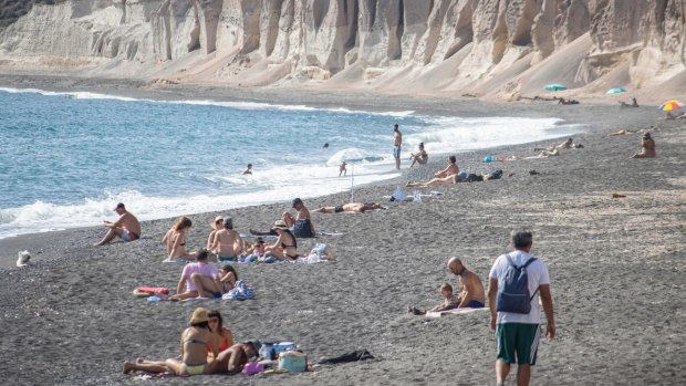 Tourists are seen relaxing, sunbathing and swimming at Vlichada Beach in Santorini.