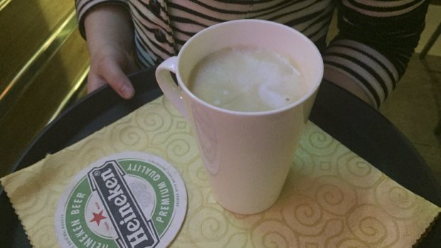 A waitress holds a caramel macchiato at a popular coffee shop in Pyongyang, North Korea, where a Heineken coaster points to more Western consumption habits.