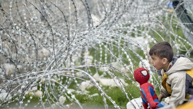 A boy stands next to razor wire around the fence between Greece and Macedonia.
