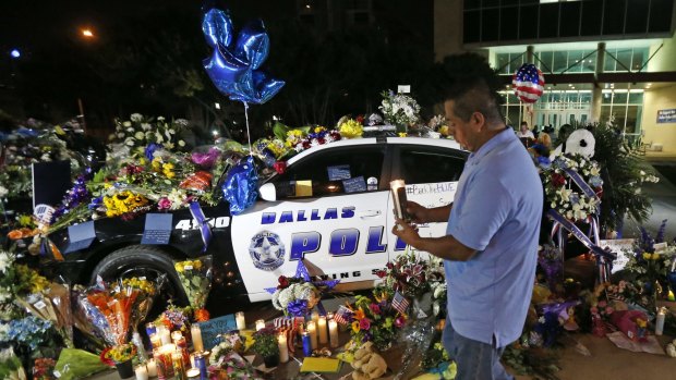 Alejandro Rodriguez places a candle in front of police cars decorated as a public memorial outside Dallas police headquarters, in memory of police who were shot Thursday in the city. 