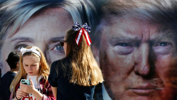 People pause near a bus adorned with large photos of candidates Hillary Clinton and Donald Trump before the presidential debate at Hofstra University in Hempstead, New York.