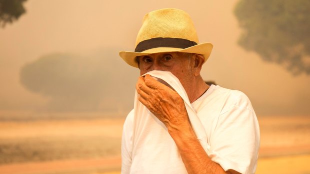 A man covers his nose and mouth from the smoke of a forest fire near Mazagon in southern Spain.