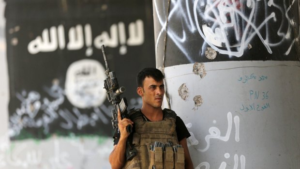 An Iraqi soldier stands  near Islamic State graffiti in Fallujah, Iraq.
