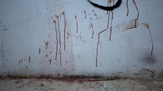 Blood splatters stain a concrete wall and the sand below on a public walkway to the beach next to the club.