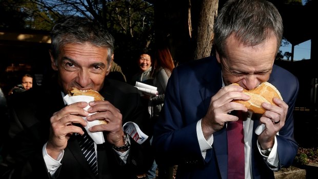 Opposition Leader Bill Shorten eats a sausage with ALP candidate for Reid, Angelo Tsirekas, during a visit to the polling booth at Strathfield North Public School on Saturday.