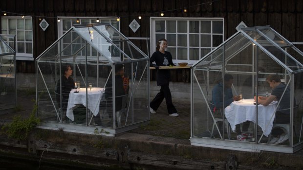 Staff at the Mediamatic restaurant serve food to volunteers seated in small glasshouses during a try-out of a setup which respects social distancing.