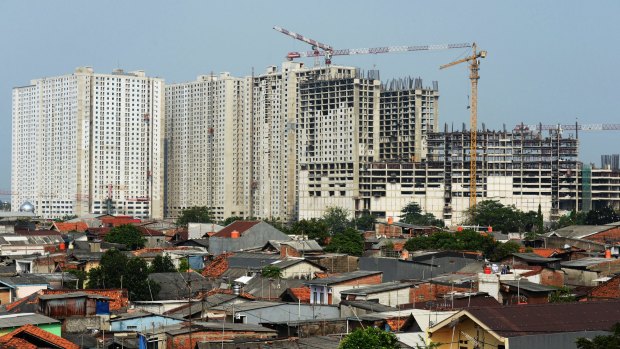 Cranes operate on residential apartment buildings under construction behind shanty houses standing in Jakarta last month. 