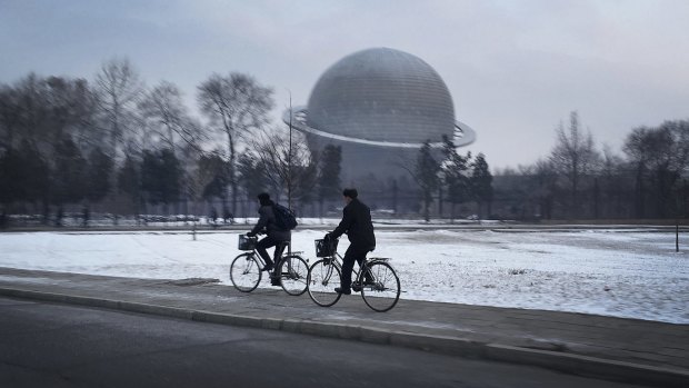 North Koreans cycle past a planetarium at the Three Revolutions Exhibition Hall on Tuesday in Pyongyang.