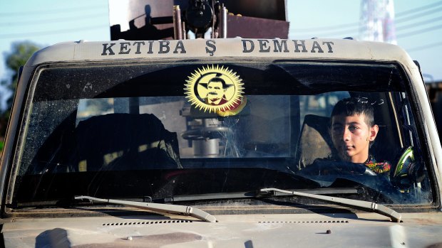 A young YPG fighter sits in a car in the village of Tel Marouf, the face of PKK founder Abdullah Ocalan on the windscreen. 
 