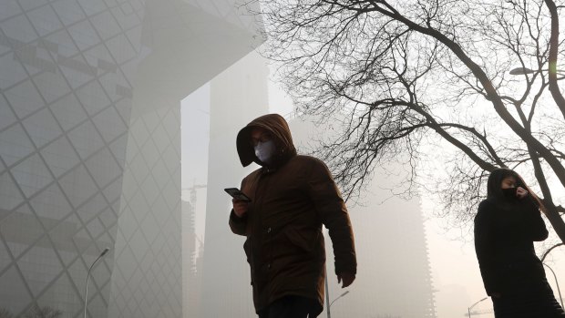 People wearing protection masks walk near the iconic headquarters of China's state broadcaster Central China Television in Beijing on Tuesday.