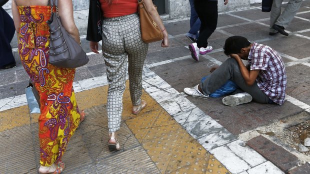 A man sits and begs for money, as pedestrians walk by outside of a National Bank, in central Athens on Tuesday. 