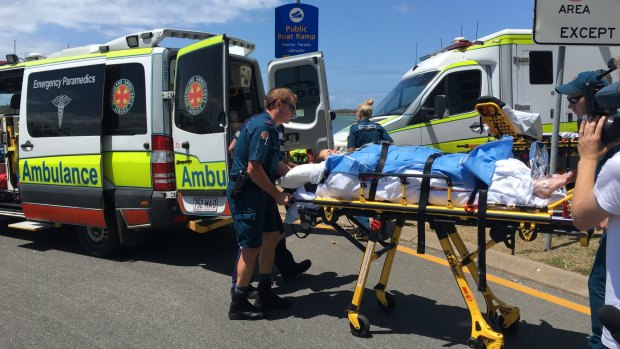 A woman is loaded onto an ambulance following the boat fire at Tipplers Beach.