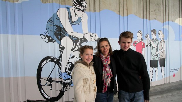 Leslie Karayan, a cyclist who lost his life when a truck hit the Annerley Road rail  bridge in Dutton Park two years ago, has been commemorated at the site with a street mural. His wife Kerri Karayan and two kids Sabine, 10, and Alessandro, 13, stand in front of the mural that depicts their dad and the family as well as other cycling friends, at the unveiling on Saturday.