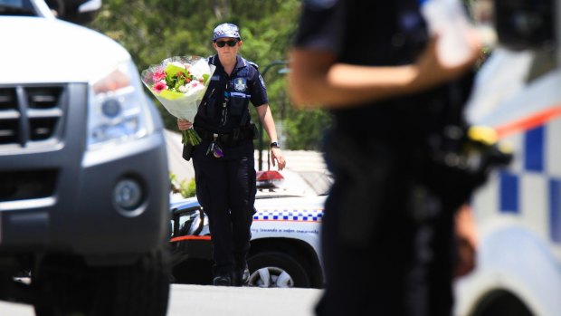 A police officer takes flowers delivered by a neighbour to the scene where Ms Bradford and her estranged husband's bodies were found.