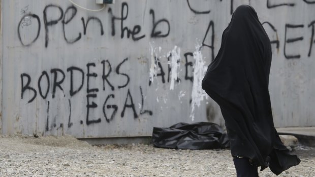 A woman walks past graffiti written on a container in Idomeni, Greece.