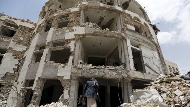 A Houthi militant walks in front of a government compound, destroyed by recent Saudi-led air strikes in Yemen.