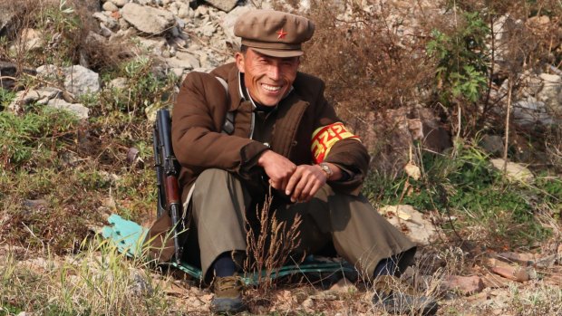 A North Korean soldier responds to Chinese tourists on the river separating them.