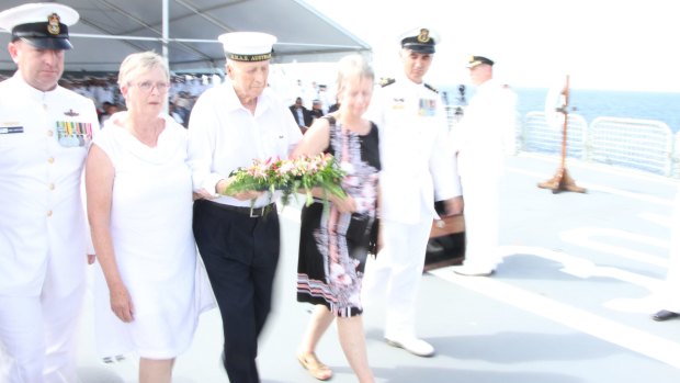 Bill Quinn, flanked by his two daughters, carries a wreath to drop on the watery grave of 84 Australians who died after HMAS Canberra sank during World War II.