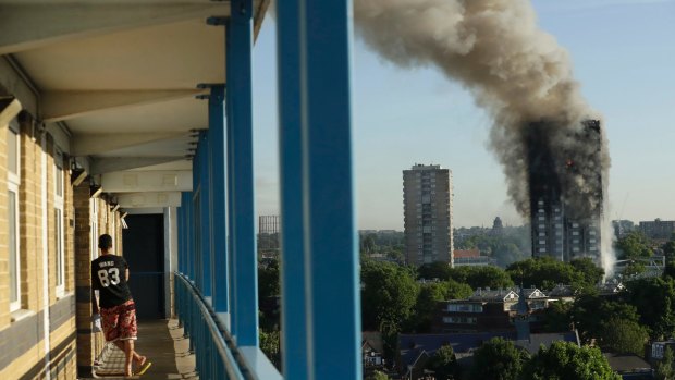 A resident in a nearby building watches smoke rise from the tower on fire in London.