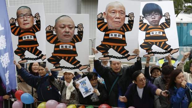 Anti-occupy Central protesters lift posters of jailed prisoners' illustrations with portraits of protest leaders, from left, Chan Kin-man, Benny Tai Yiu-ting, Chu Yiu-ming and Joshua Wong, outside the police station in Hong Kong.